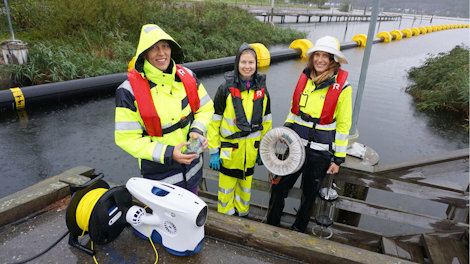 tre personer i regntøy, bak undervannsdrone.