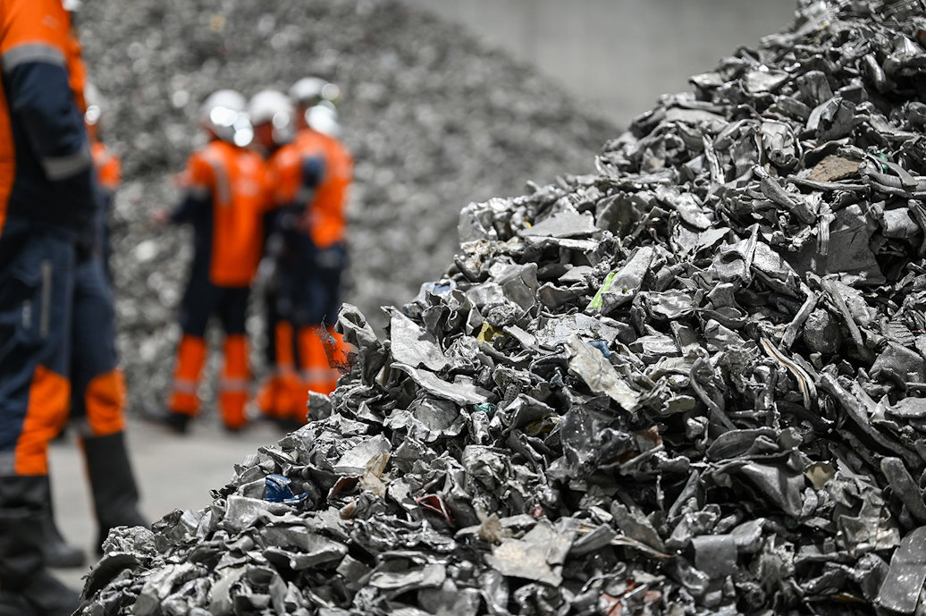 a group of workers in orange vests standing next to a pile of aluminium scrap